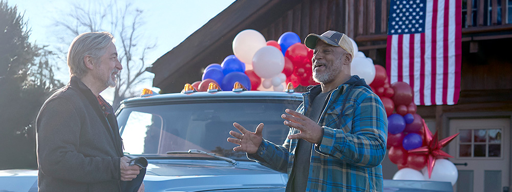 two American Veterans talking with an American Flag and red white and blue balloons in the background